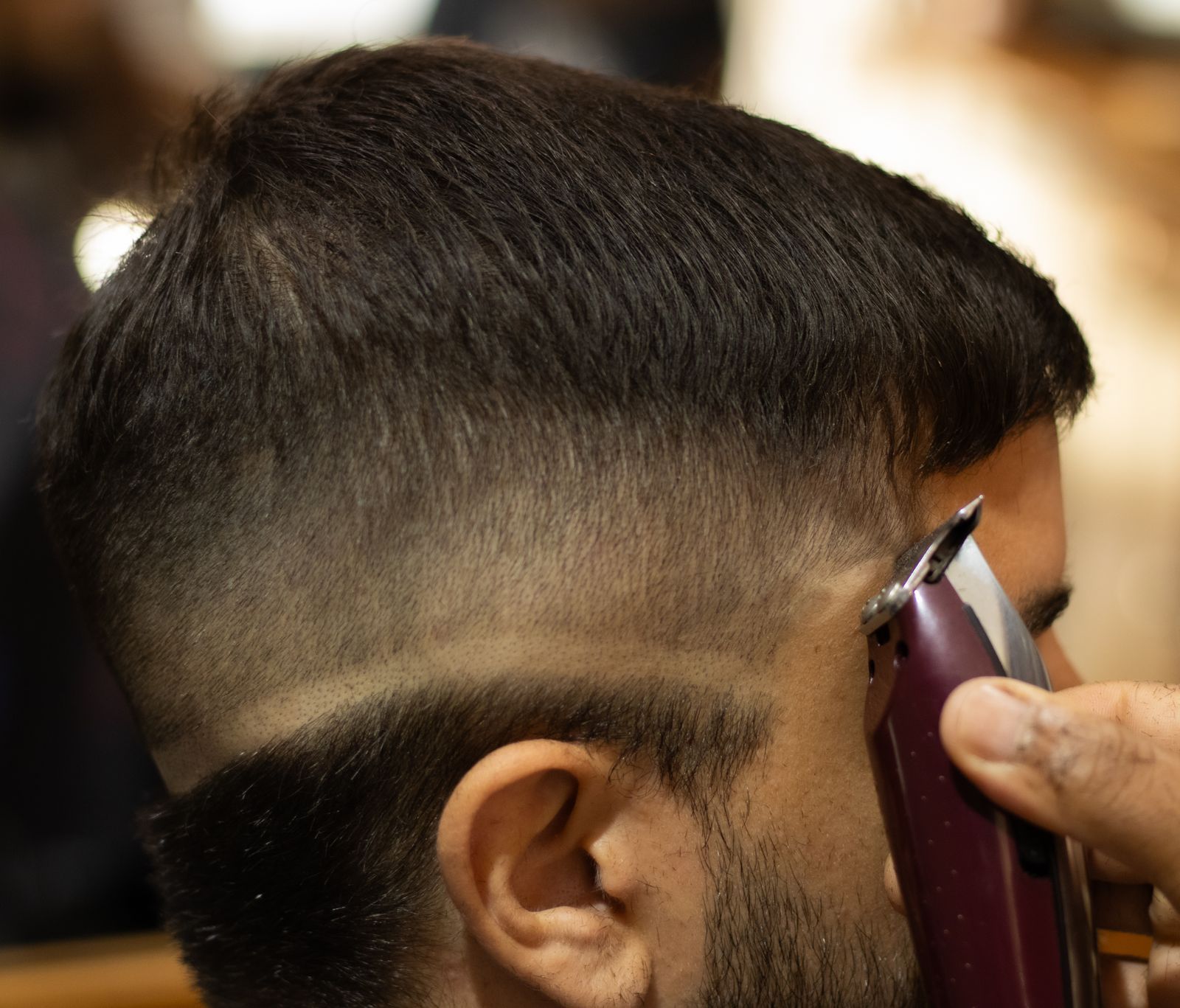 A barber's clipper finishing a skin fade on the side of a client's head.
