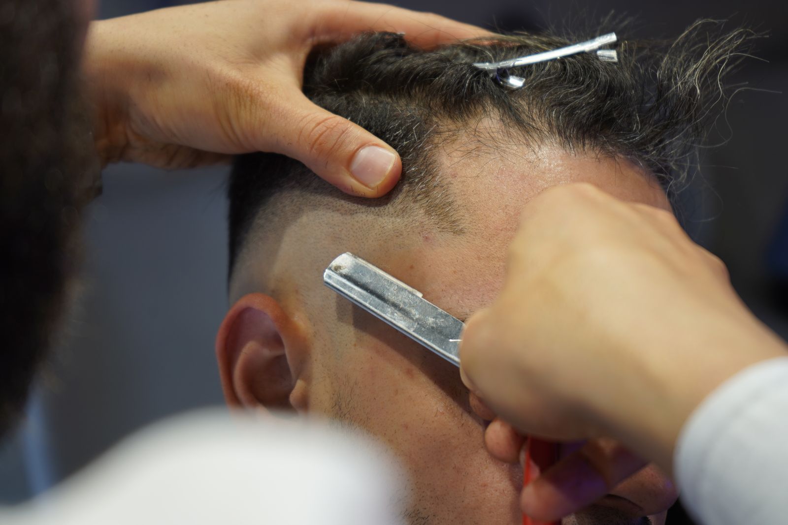 A barber holds the hair back while shaving a part line with a straight razor.