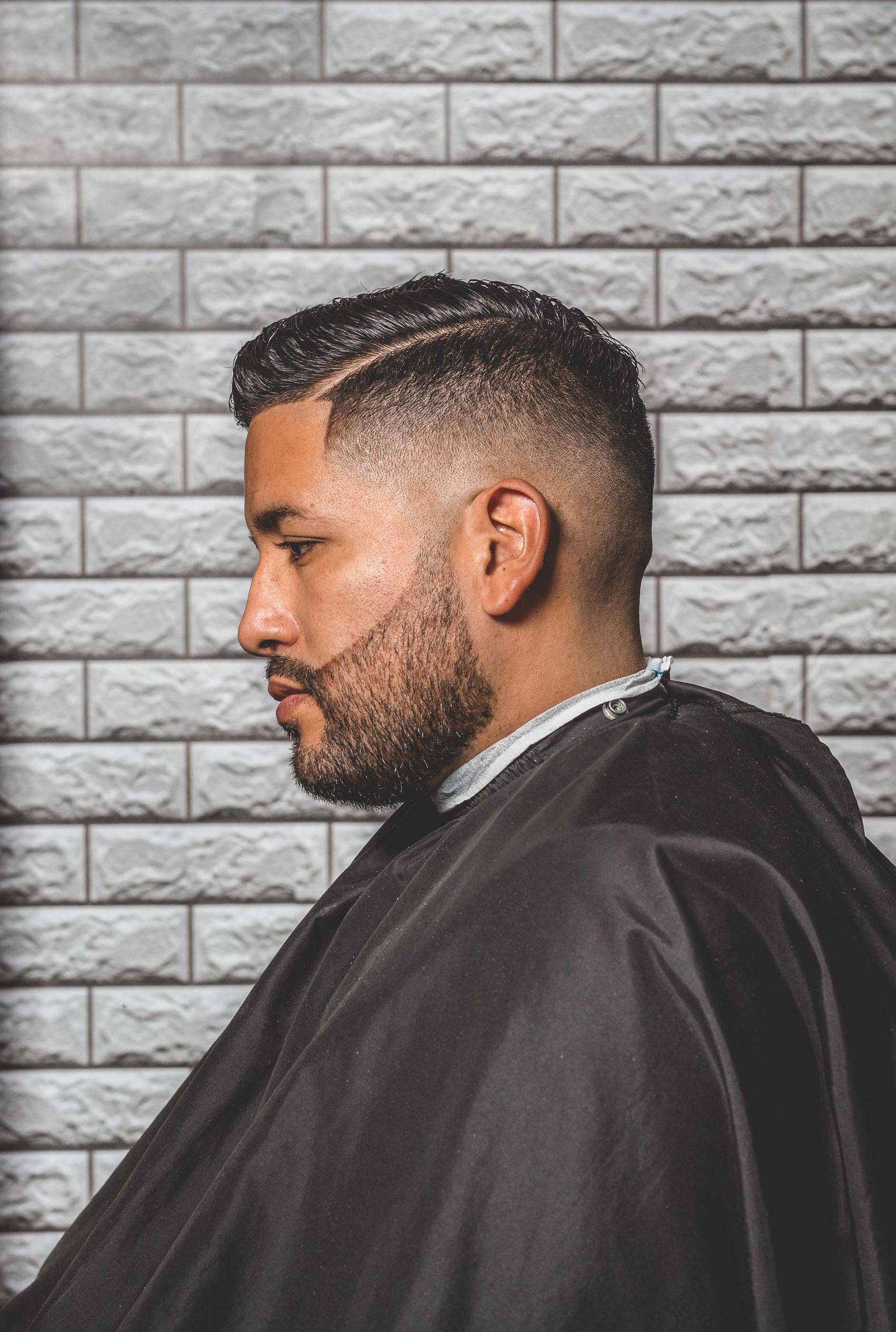 A client in profile with a side part, a high fade and a full trimmed beard.